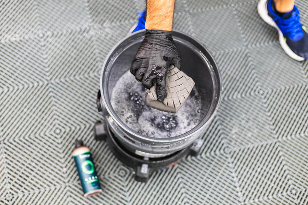 A closeup of a person squeezing a black Ultra Sponge over a bucket filled with water and bubbles.