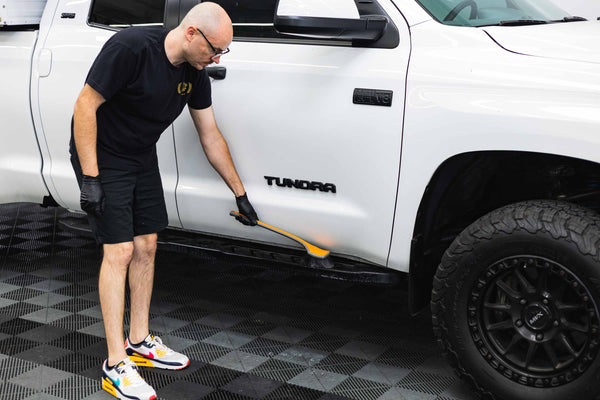 Person cleaning a white Toyota Tundra truck with a Detail Fender Well Brush solar flare.