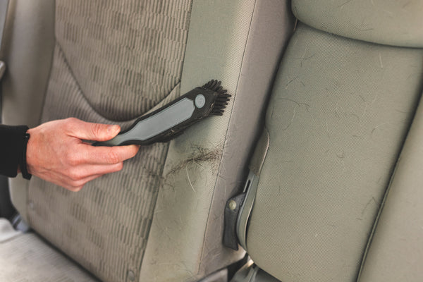 A hand cleaning a car seat with the Detail Factory Pet Hair Brush.
