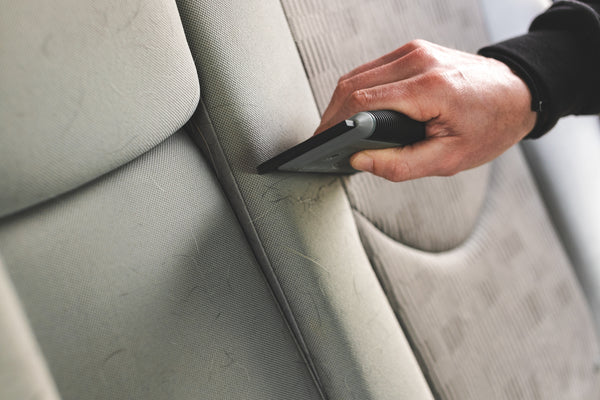 A person cleaning a car seat with the Detail Factory Pet Hair Card