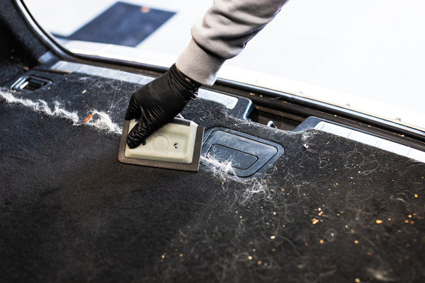 A person using the Detail Factory Pet Hair card to remove hair from the trunk of a vehicle.
