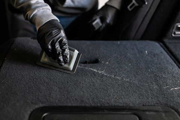 A person using the Detail Factory Pet Hair card to remove hair from the back of seats of a vehicle.