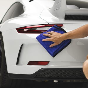 Using a royal blue Dry Me A River towel from The Rag Company to wipe the bumper of a white Porsche 911 GT3 sports car