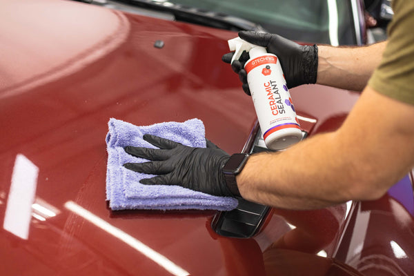 Gtechniq C2V Ceramic Sealant bottle spraying on the hood of a car being wiped with a purple towel.