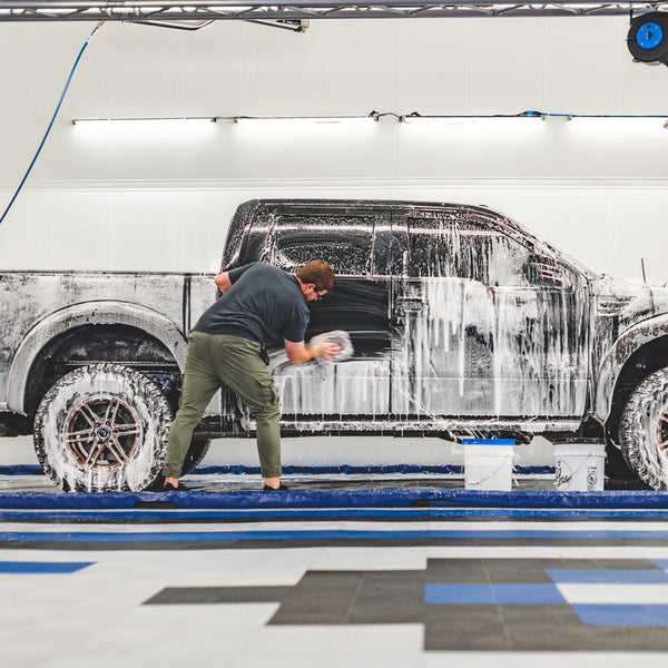 A person wiping white foam off the back door of a black Ford Raptor.