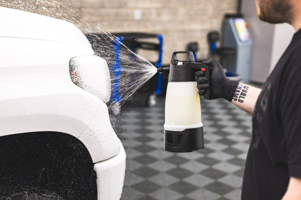 A man spraying cleaner onto a headlight using an iK Foam sprayer.