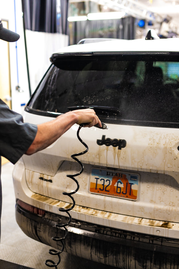A person using an IK Sprayer to clean off the back of a very dirty Jeep Cherokee.