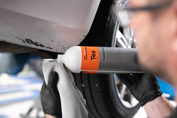 A person adding a dollop of Koch Chemie Tea to the corner of a towel before scrubbing grime off the bottom of a car.