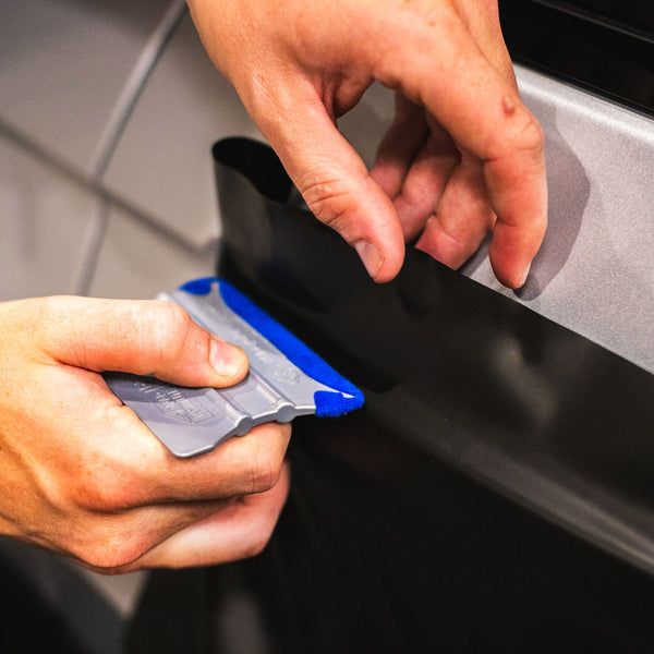 A hand using the blue Monkey Strip to lay vinyl on a car door handle.