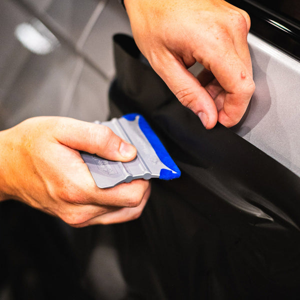 A hand using the blue Monkey Strip to lay vinyl on a car door handle.