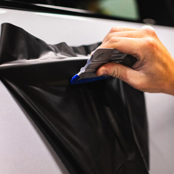 A hand using the blue Monkey Strip to lay vinyl on a car door handle.