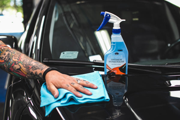 An image of a person rubbing the hood of a black car with a blue Rip N' Rag with a spray bottle of Optimum Hyper Polish showcased behind.
