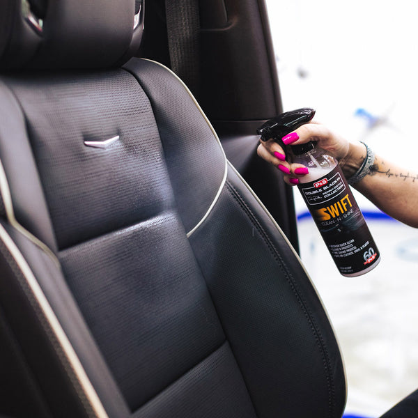 A hand with a neon pink manicure spraying a car seat with P & S Swift Interior Clean and Shine.