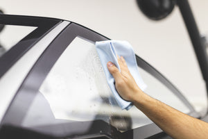 Using a blue Premium Glass & Window microfiber towel from The Rag Company to clean the windshield of a boat