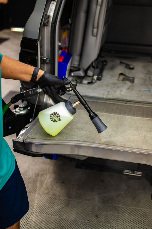 A person using an Ultra Air Blaster plus to clean the carpet in the back of a vehicle.