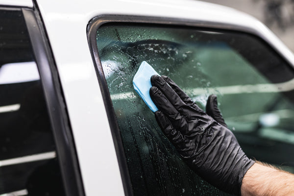 A gloved hand using a Ultra Clay bar on the window of a white vehicle.