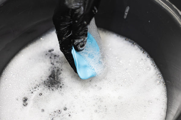 The Rag Company Ultra Clay Bar being dumped into a soapy bucket.