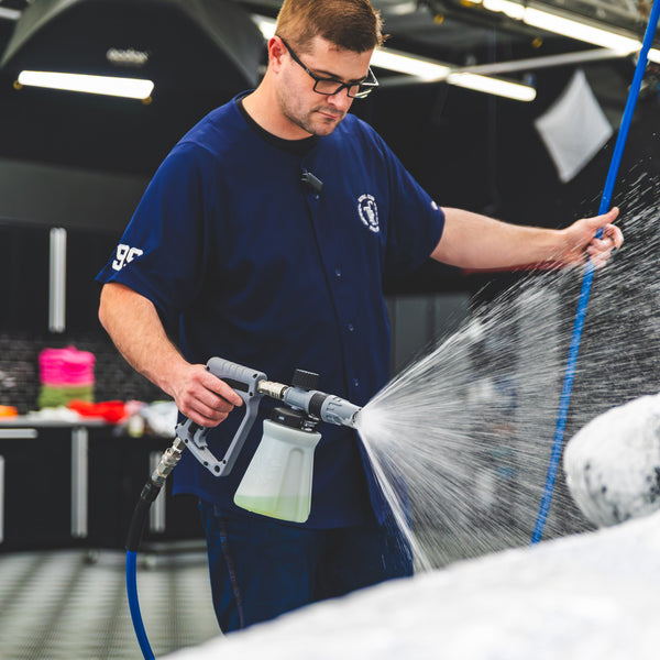 A person using a TRC Ultra H2O Foam Cannon to spray soap onto a blue car.