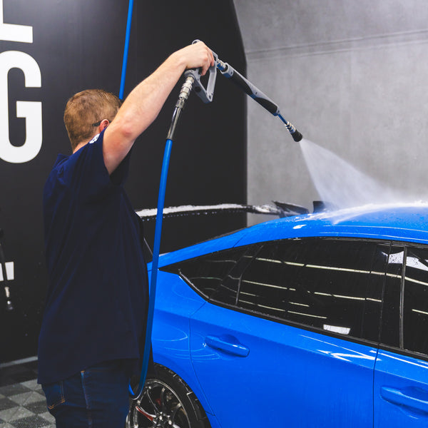 A person spraying water onto a blue car using a TRC Ultra H2O Spray Wand.