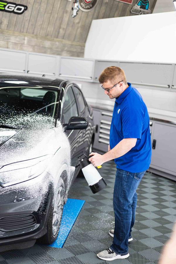 A man using an iK sprayer to spray a cleaner onto a car.
