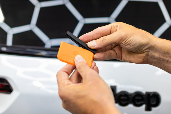 A person using the Yellotools Yelloblade on the back window of an SUV.