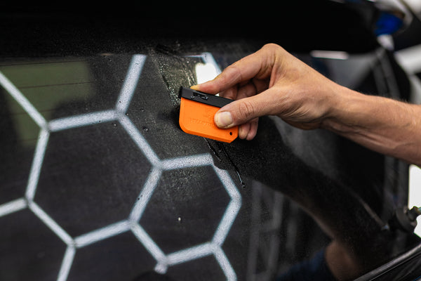 A person using the Yellotools Yelloblade on the back window of an SUV.