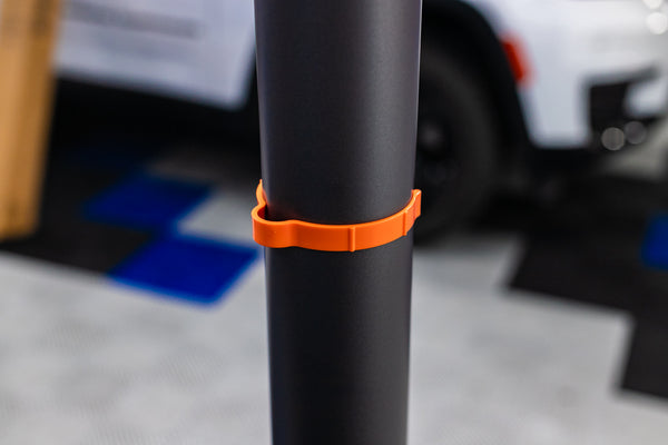 An orange Yellotool Speedclip on a black pole with a car in the background.