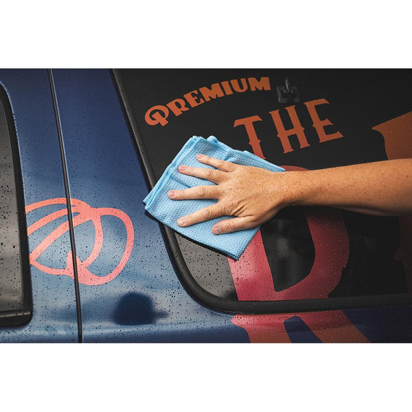 A person scrubbing a car door with a blue standard waffle weave towel.