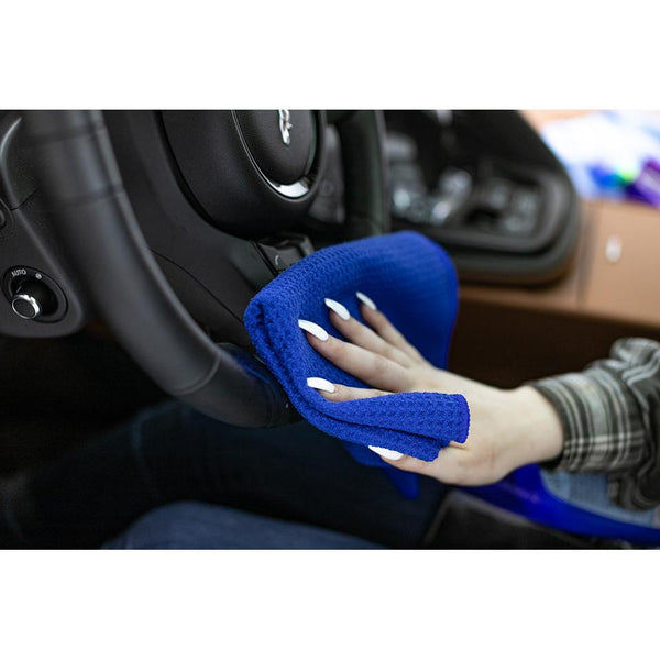 A person wiping a car steering wheel with a blue standard waffle weave towel.