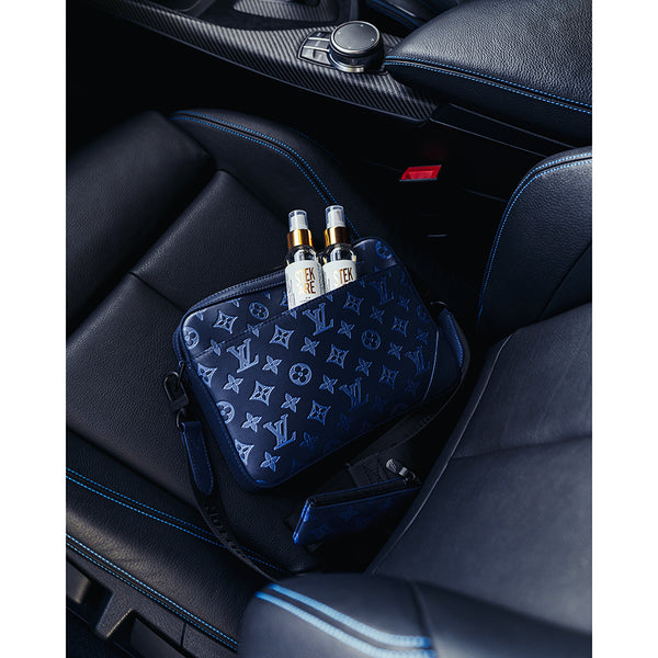 A black Luis Vuitton bag with two bottles of Stjarnagloss Stekare in it. The bag is laying on a car's black leather seat.