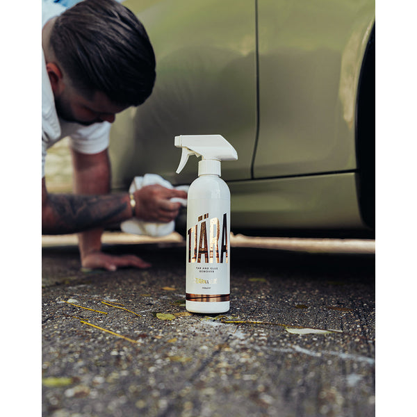 A spray bottle of Stjarnagloss tar and glue Remover with a background of a person detailing the bottom of their car.