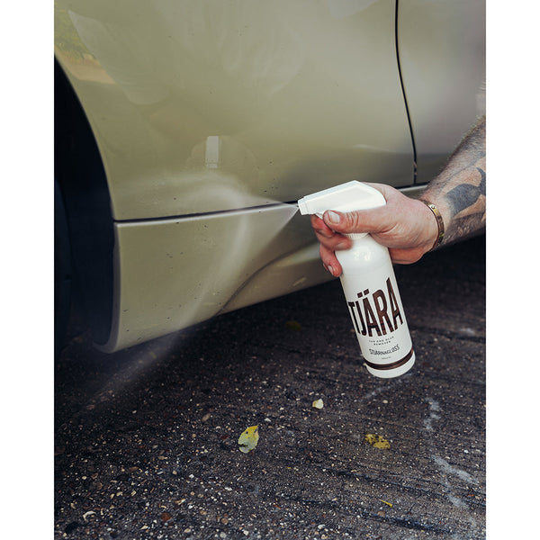 A closeup of a person spraying Stjarnagloss Tar and Glue Remover on the bottom of a beige car.