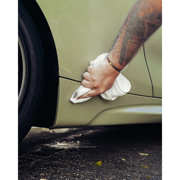 A closeup of a person detailing the bottom of a beige car with a white towel.