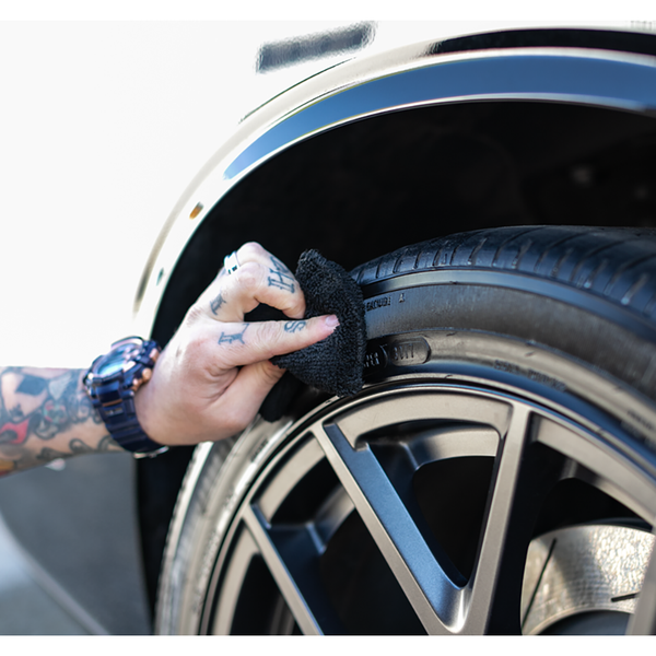 A closeup of a person scrubbing a tire with a blacks terry sponge.