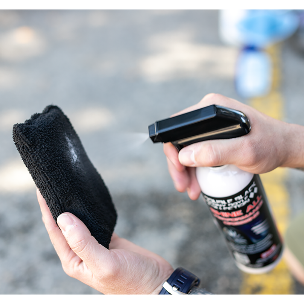 A closeup of a person spraying P & S Shine All onto a black terry sponge.