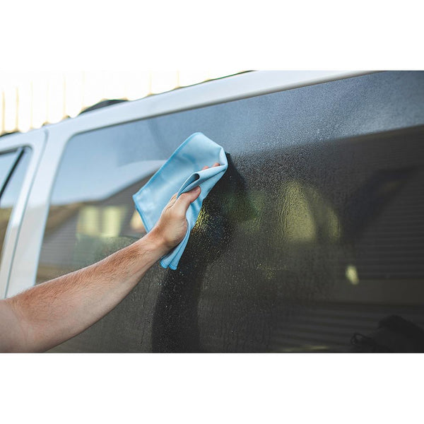 A closeup of a person wiping a car window with a blue glass towel.