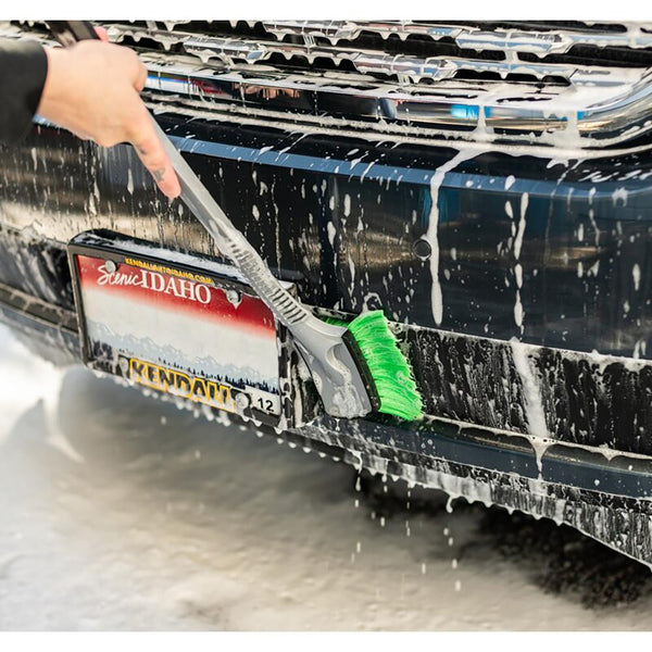 A closeup of a person scrubbing the bumper of their car with a green bristle Wheel and Body Brush.