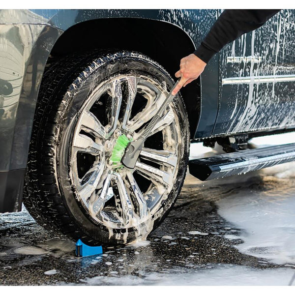 A closeup of a person scrubbing the tire of their car with a green bristle Wheel and Body Brush.