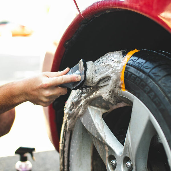 A closeup of a person scrubbing a tire with a Tire Brush.