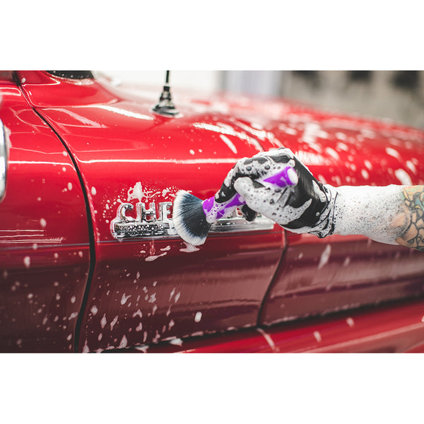 A closeup of a person cleaning the emblem on the side of their truck with a purple synthetic detailing brush.