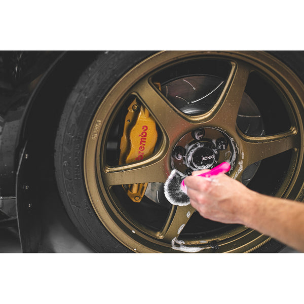 A closeup of someone detailing a tire rim with a pink synthetic detailing brush.