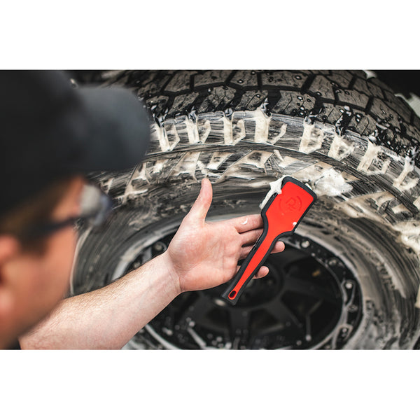 A closeup of a person scrubbing a tire with a red Detail Factory Tire Scrub Brush.