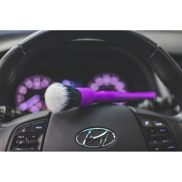 A purple synthetic detailing brush on top of a steering wheel.