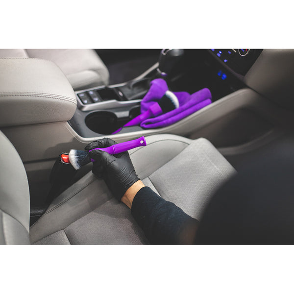 A closeup of a person detailing a seatbelt with a purple synthetic detailing brush.