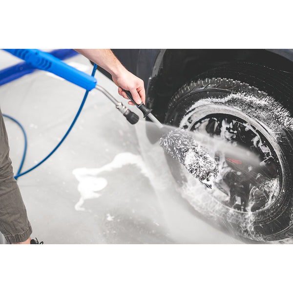 A closeup of a person a car tire with a pressure washer.