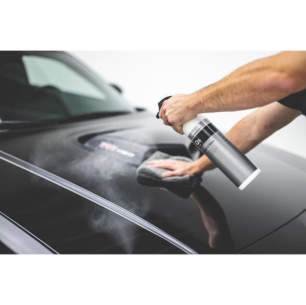 A closeup of a person spraying the hood of a black car with Koch Chemie Quick and Shine and wiping it with a grey towel.