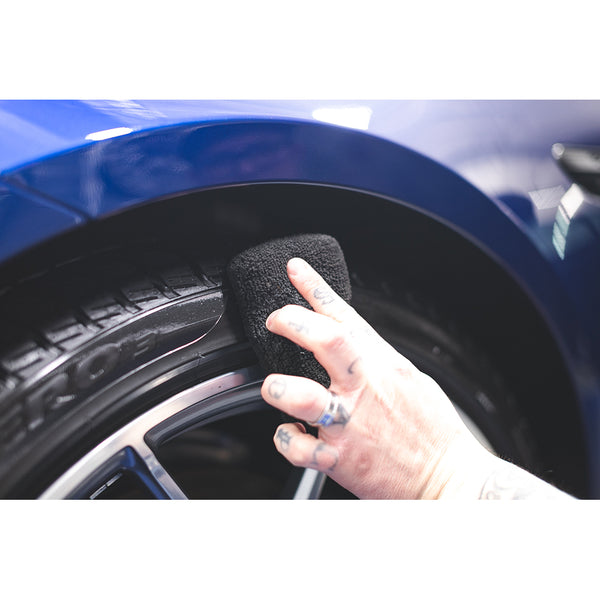 A closeup of a person scrubbing a car tire with a black Terry Sponge.