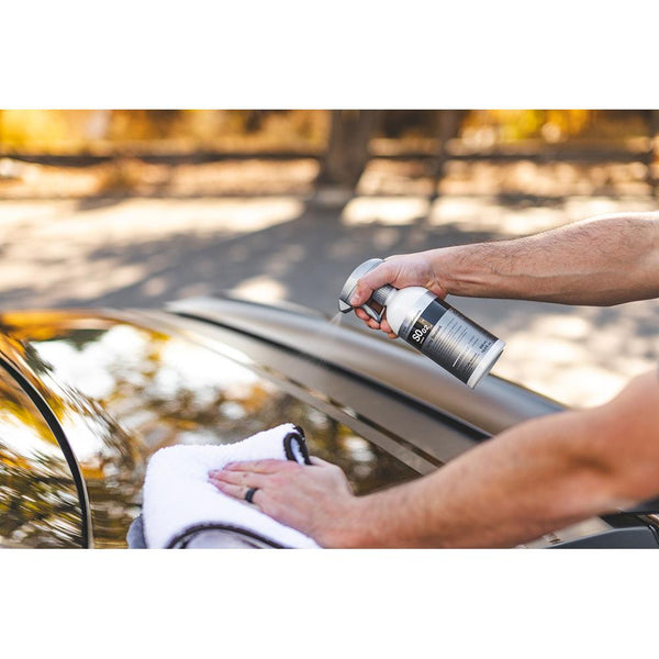A person spraying the back of a car with Koch Chemie Spray Sealant and wiping it with a white towel.