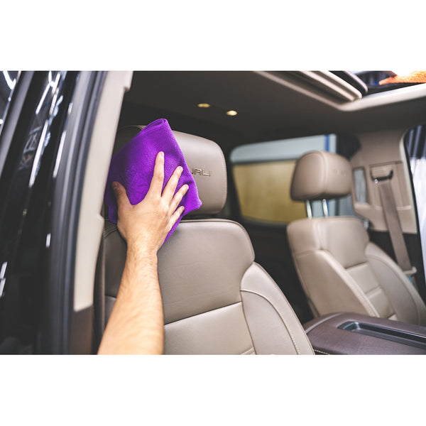 A person scrubbing a leather head rest with a purple towel.