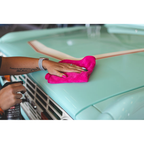 A closeup of a person scrubbing a teal car hood with a pink towel.